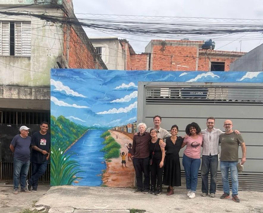 Membros do consórcio reunidos em frente ao mural do Jardim Pantanal, que retrata crianças brincando na chuva à beira do Rio Tietê.